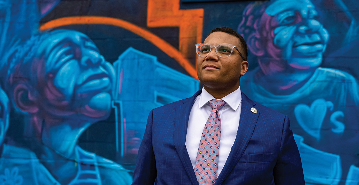 Photo of Brandon Taylor in front of community mural, looking skyward in inspiration