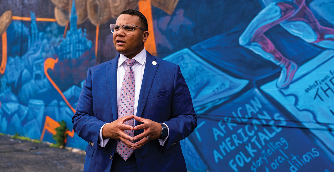 Photo of Brandon Taylor in front of community mural, looking to his right, mid-conversation